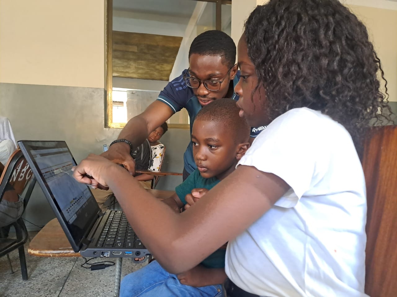 A Mikrobot facilitator guiding two students through a programming exercise on a laptop
